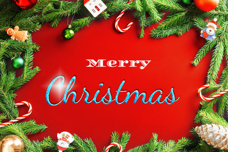 A vibrant red Christmas background framed by green fir branches and festive holiday ornaments with "Merry Christmas" text. High quality photoの写真素材
