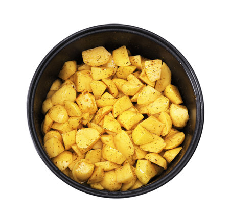 An overhead close-up of raw, diced yellow potatoes tossed with black pepper and spices inside the black pot of a multi-cooker. High quality photoの写真素材