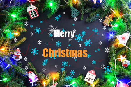 Merry Christmas text framed by illuminated fir branches, gingerbread figures, and small wooden houses on a dark background. High quality photoの写真素材