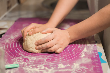 A close-up shot of hands kneading a fresh ball of white dough on a purple silicone baking mat in a kitchen setting. High quality photoの写真素材