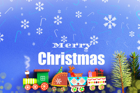 A Christmas background with "Merry Christmas" text, snowflakes, and a colorful wooden toy train with gifts on a blue surface. High quality photoの写真素材