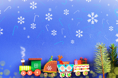 Toy Christmas train carrying gifts, a reindeer, and a fir tree on a blue background with snowflakes and candy cane patterns. High quality photoの写真素材