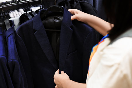 A shopper's hands examining a dark blue or navy blazer suit jacket hanging on a rack in a clothing retail store. High quality photoの写真素材