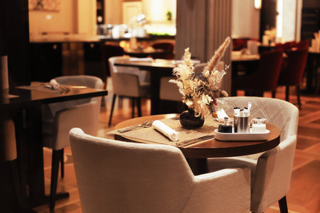 An intimate table setting in a luxury restaurant with a floral centerpiece, plush chairs, and warm ambient lighting. High quality photoの写真素材