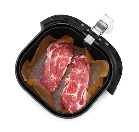 An overhead view of two raw pork neck steaks seasoned and lined with parchment paper inside the basket of a black air fryer. High quality photoの写真素材