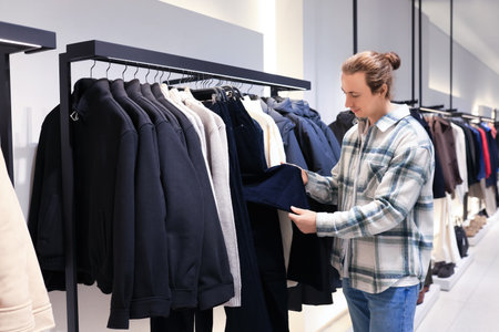 man choosing clothes in fashion store. Male customer inspecting trousers on rack at shopping mall. High quality photoの写真素材