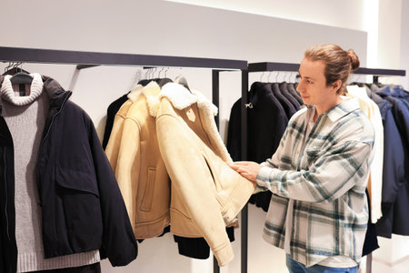 man winter browsing clothes in a fashion store, examining a beige shearling jacket on a rack. High quality photoの写真素材