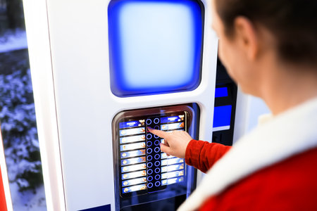 A man selects a hot drink from a street vending machine against a backdrop of winter snow. High...