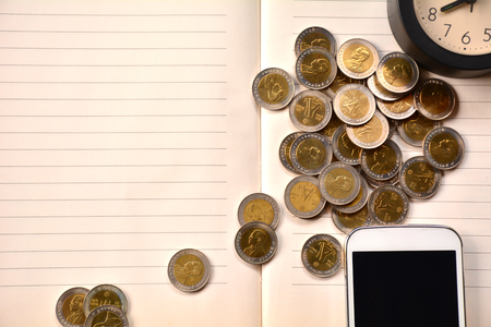 Coins, smart phone and clock put on notebook.の写真素材