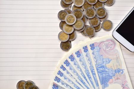 Coins, smart phone and fifty baht bill put on notebook.
