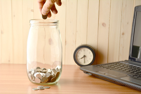 Men drop coin into the bottle, alarm clock and laptop on the table.の写真素材