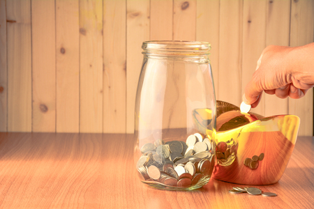 Man drop coins into the gold money box, big glass bottle.の写真素材