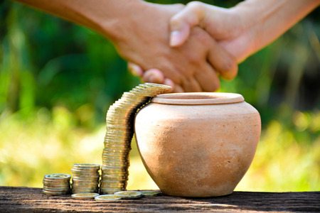 The old earth ware and coin stack almost drop in earth ware and hand of people shake hand
