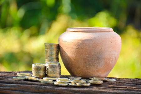The old earth ware and coin stack on nature blur backgroundの写真素材