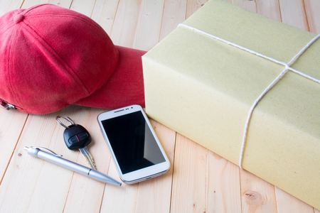 The red cap, parcel post, white paper, pen, smart phone and key of car on bark tableの写真素材