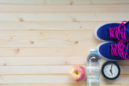 Sport shoes, apple, white tape measure, alarm clock and plastic bottle for exercise and healthy on wood table top viewの写真素材