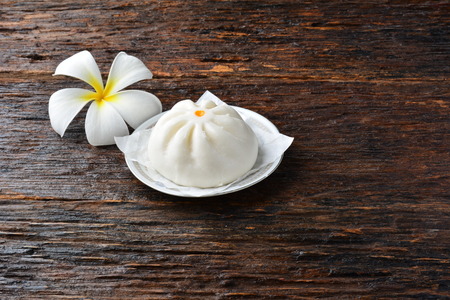 White Chinese bun on a plate and white flower on brown wood table under the nature lightの写真素材