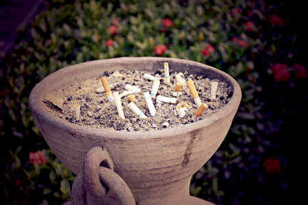 The used cigarettes place on sand in the big stone pot in publicの写真素材