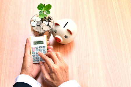 Finance, hand of person using calculator with coins in glass and white piggy bankの写真素材