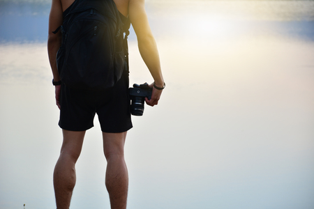 man stand beside lake and holding camera and sun light reflect on water