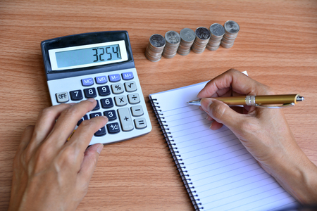 person writing and using calculator beside stack coins for finance and businessの写真素材