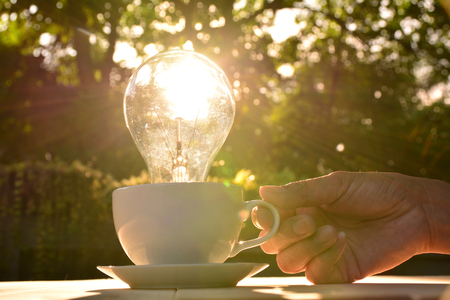 idea concept with light bulbs in coffee cup and hand of human holding cup on nature background.の写真素材