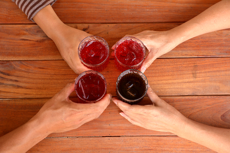 hand of people holding a glass of sweet drink with ice cubes on wooden table background.の写真素材