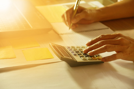 Hand using calculator and holding pencil for analyzing financial data and counting on document.の写真素材