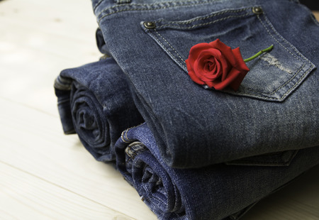 Blue jeans folded with red rose on wooden table and on wooden background.の写真素材