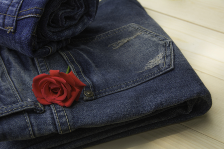 Blue jeans folded with red rose on wooden table and on wooden background.の写真素材