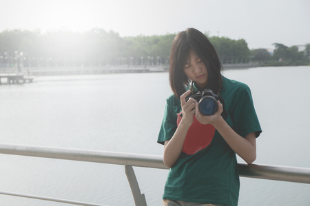 Smiling young woman using a camera to take photo outdoors at the parkの写真素材