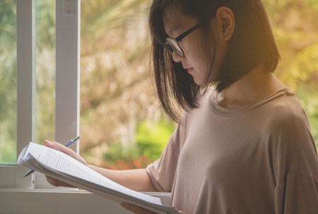 woman wearing glasses sitting and holding paper sheet and reading an examの写真素材