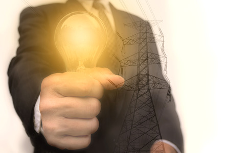 Double exposure close up of businessman hands holding glass light bulb with electricity post.の写真素材