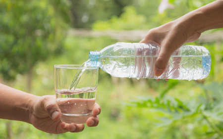 Female hand pouring water from bottle to glass on nature backgroundの写真素材