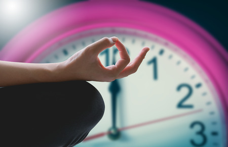 Close-up of feminine and masculine arms and crossed legs during meditation with clock background.の写真素材