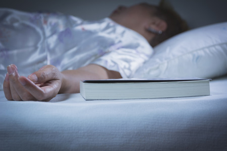 Woman sleeping with a book on the bed in bedroom, she is resting with eyes closed.の写真素材