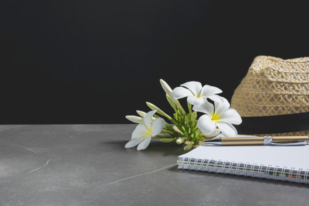 Open notebook with hat. Book open, with pen and flower on table dark tone background.の写真素材