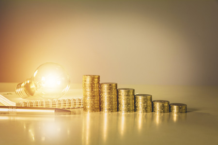 Energy saving light bulb and stacks of coins on table. Financial and saving concept.の写真素材