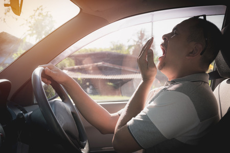 Sleepy yawning man driving car in traffic after long hour drive. Man falling asleep in car.の写真素材