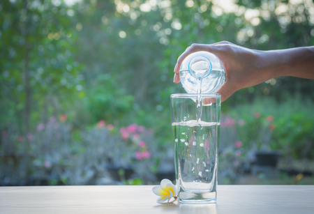 Female hand pouring water from bottle to glass on nature backgroundの写真素材