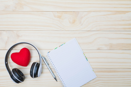 Red heart with headset, pen and empty note on wooden table with copy space for valentine day concept.の写真素材