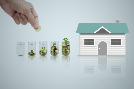 Hand of man holding coin and drop into the glass. Save money for a house concept.の写真素材
