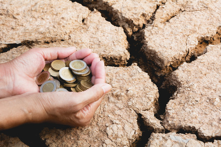 Hand holding coins money in hand on drought area background. Financial, accounting and saving...