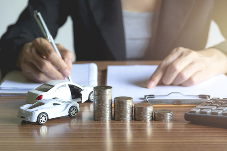 Car insurance and car service. Businesswoman with stack of coins and toy car, business and financial concept.の写真素材