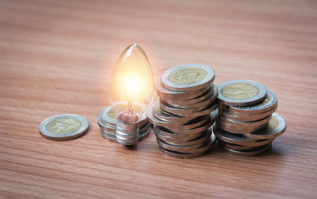 Energy saving light bulb and tree growing on stacks of coins on nature background. Saving, accounting and financial concept.の写真素材