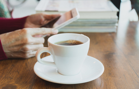 Female using a tablet with tea cup on wooden table.