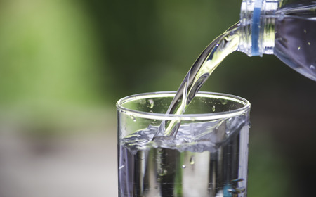 Female hand pouring water from bottle to glass on blur background