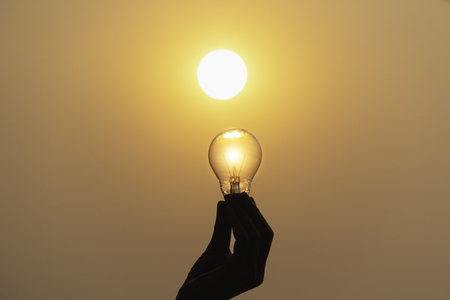 Hand hold a light bulb on sunset background for saving energy and creative concept.