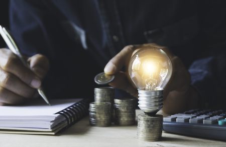 Man working with a light bulb on stack of coins for business and accounting concept.の写真素材