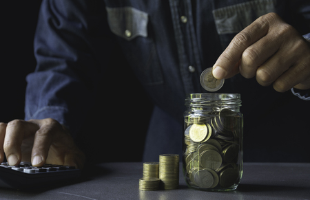 Saving money concept and hand putting money coin in the glass jar for financial and accounting concept.の写真素材